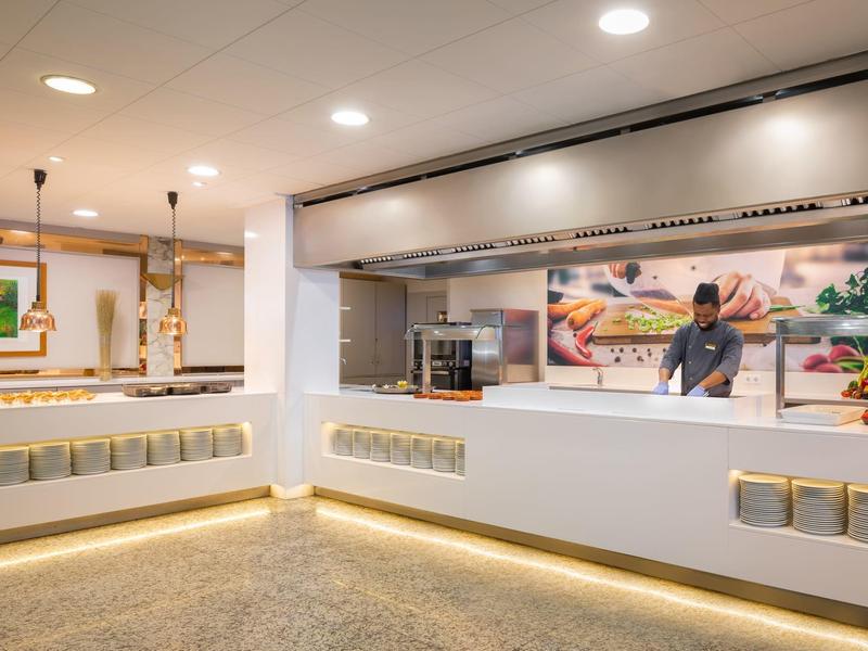 Cucina moderna dell'hotel con bancone aperto, illuminazione e personale di cucina sullo sfondo.