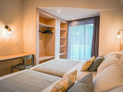 Modernes Hotelzimmer mit Doppelbett, Schreibtisch, offenem Kleiderschrank und großem Fenster mit Vorhängen.