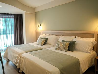 Modernes Hotelzimmer mit zwei Betten, grünen Akzenten und natürlichem Licht durch Vorhänge.