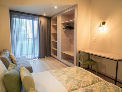 Helles Hotelzimmer mit Bett, Schreibtisch und offenem Kleiderschrank mit Handtüchern.