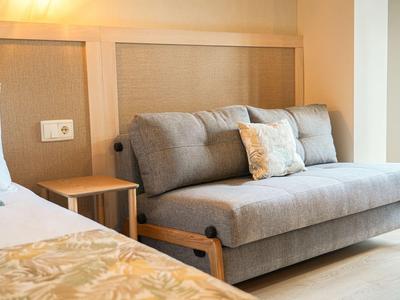 Gemütliche Sitzecke mit grauem Sofa und Kissen neben einem Bett in einem Hotelzimmer.