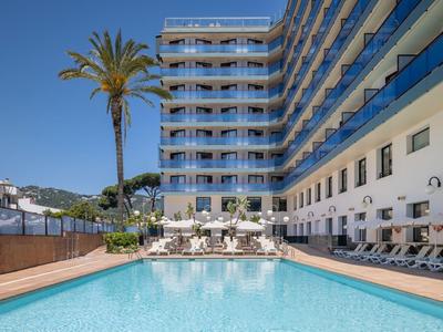 Moderner Hotelpool mit Sonnenliegen, Palmen und klarem Himmel im Hintergrund.