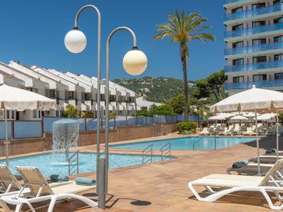 Poolbereich mit Liegestühlen und Sonnenschirmen vor einem modernen Hotel bei klarem Himmel.