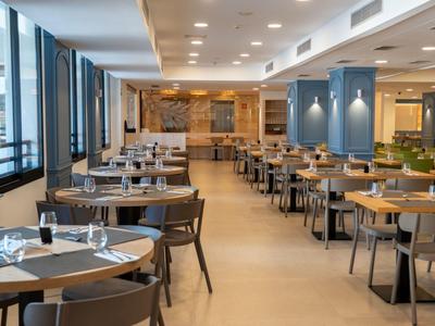 Modernes Hotelrestaurant mit Tischreihen, warmem Licht und großen Fenstern.