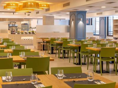Modernes Restaurant mit grünen Stühlen, Holztischen und großen gelben Deckenlampen.