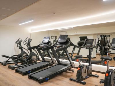 Ein Fitnessraum mit Laufbändern, Fahrrädern und Spiegeln, helle Beleuchtung und Motivationsslogan an der Wand.