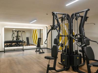 Moderner Fitnessraum mit multifunktionalen Trainingsgeräten, Spiegelwand und hellen Farben.