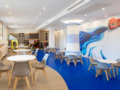 Moderner, heller Lounge-Bereich mit weißen Tischen, Holzstühlen und einem blauen Teppichboden.