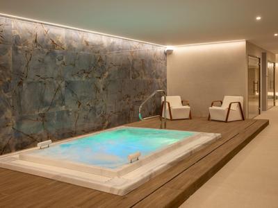 Moderner Whirlpool mit blauer LED-Beleuchtung in einem luxuriösen Hotelspa mit Sitzgelegenheiten.