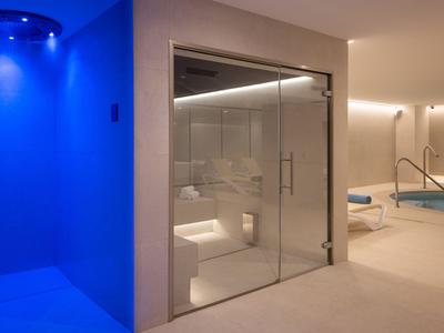 Moderner Spa-Bereich mit blauer Lichtdusche, Glasdusche und Whirlpool im Hintergrund.