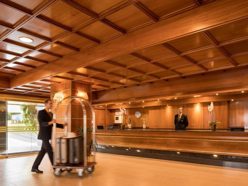 Velká hotelová hala se dřevěným stropem, recepcí a vozíkem na zavazadla.