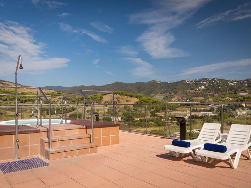Terasa s bazénem, dvěmi lehátky a výhledem na kopcovitou krajinu pod modrou oblohou.
