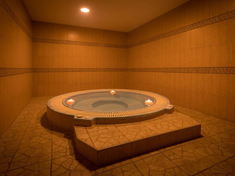 Kulaté vířivka v béžovém, teple osvětleném pokoji s obklady na stěnách a podlaze.