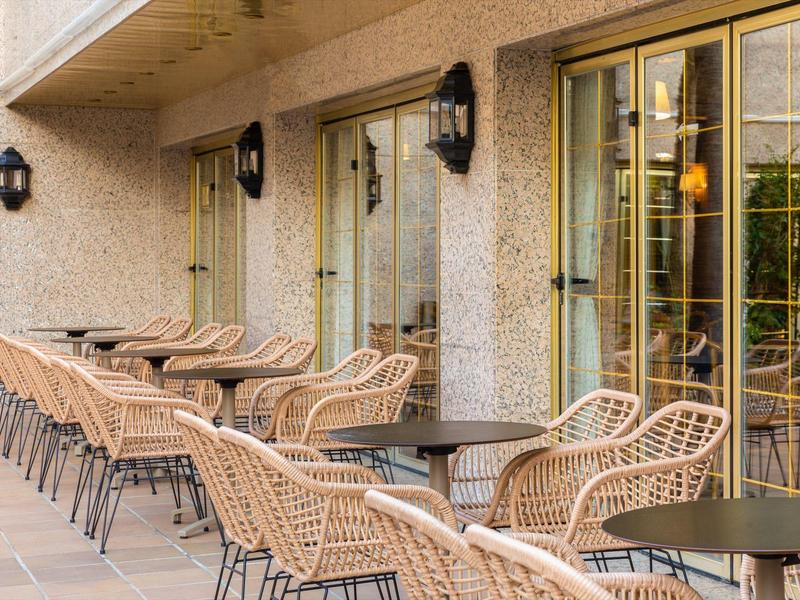 Außenterrasse mit Korbstühlen und Tischen vor Glasfenstern eines Hotels.