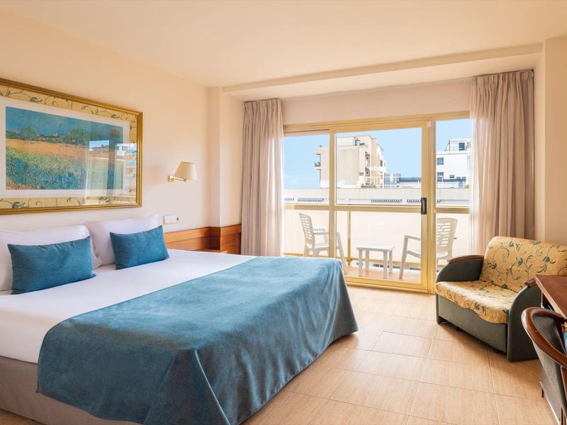 Helles Hotelzimmer mit Doppelbett und Zugang zu einem Balkon mit Meerblick.