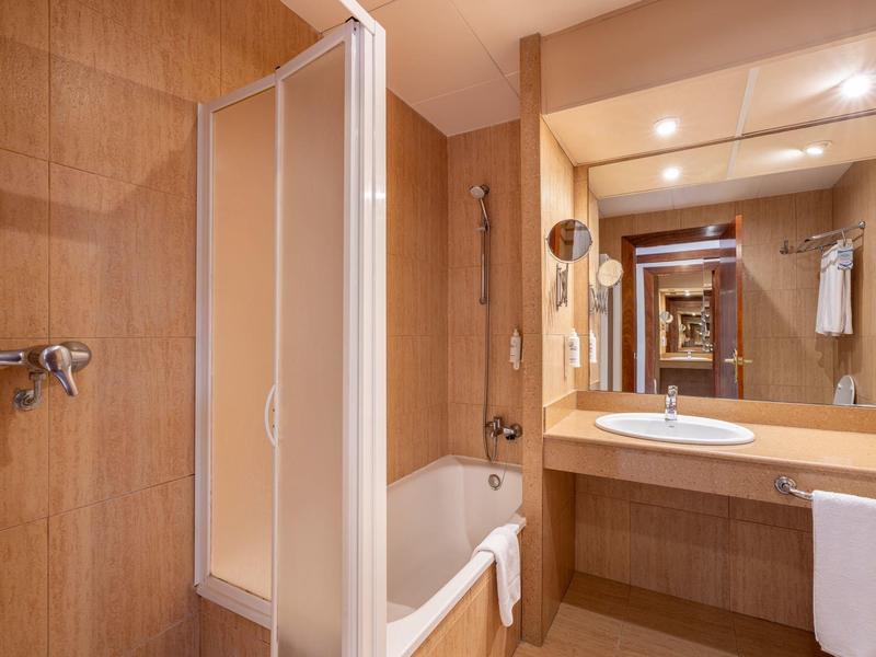 Kompaktes Badezimmer mit Badewanne, Duschabtrennung und Waschbecken unter beleuchtetem Spiegel.