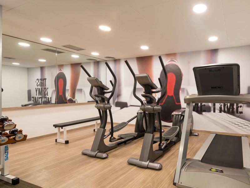 Moderner Fitnessraum mit Trainingsgeräten, Hanteln und großer Spiegelwand.