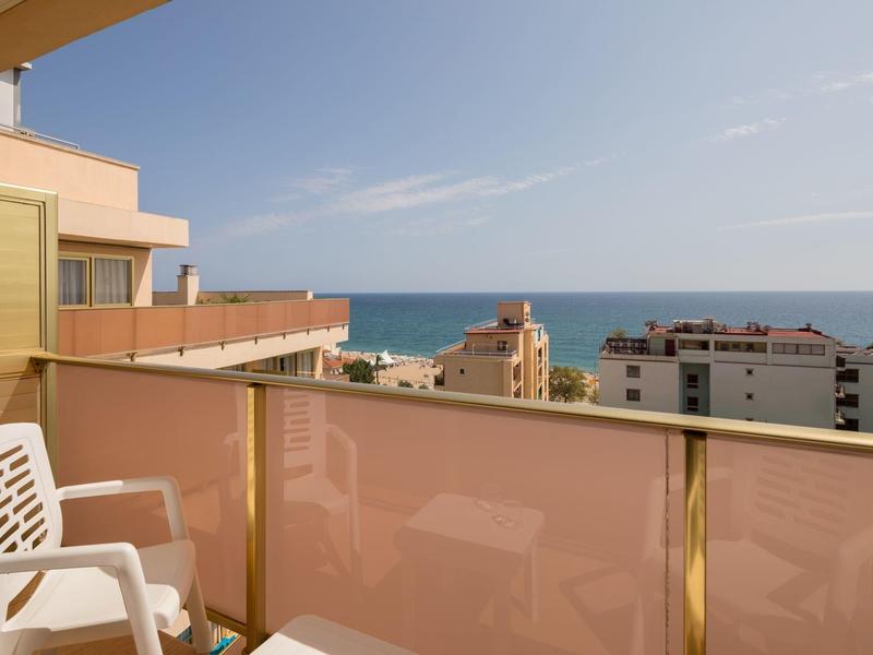Balkon mit zwei weißen Stühlen und Meerblick bei klarem Himmel.