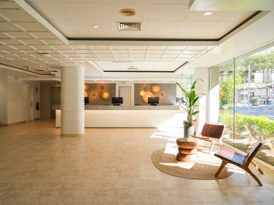 Luminoso atrio dell'hotel con banco reception, sedie e grandi finestre con vista esterna.