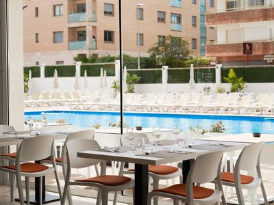 Area pranzo moderna con sedie bianche e tavoli accanto a una piscina esterna.