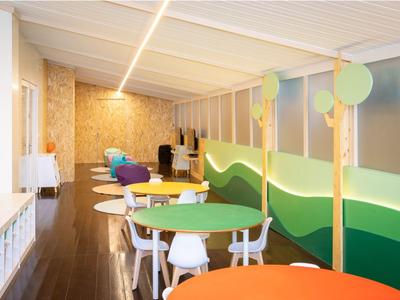 Area giochi e pranzo luminosa con tavoli colorati, sedie bianche e decorazioni murali.