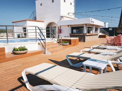 Terrasse mit Sonnenliegen, Pflanzgefäßen und einer Bar unter klarem Himmel.
