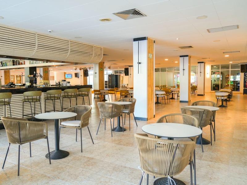 Area lounge hotel moderna con tavoli rotondi e sedie imbottite su pavimento chiaro.