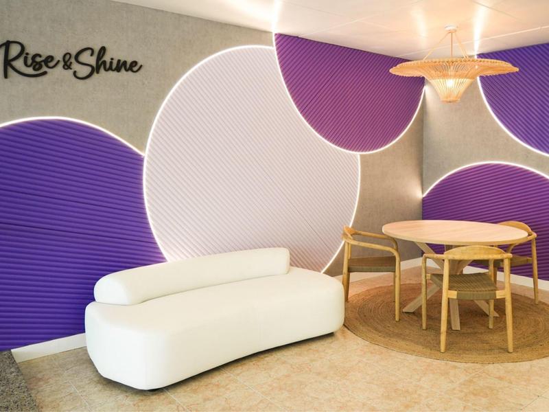 Area lounge moderna con pannelli murali viola e bianchi, divano bianco e sedie in legno.