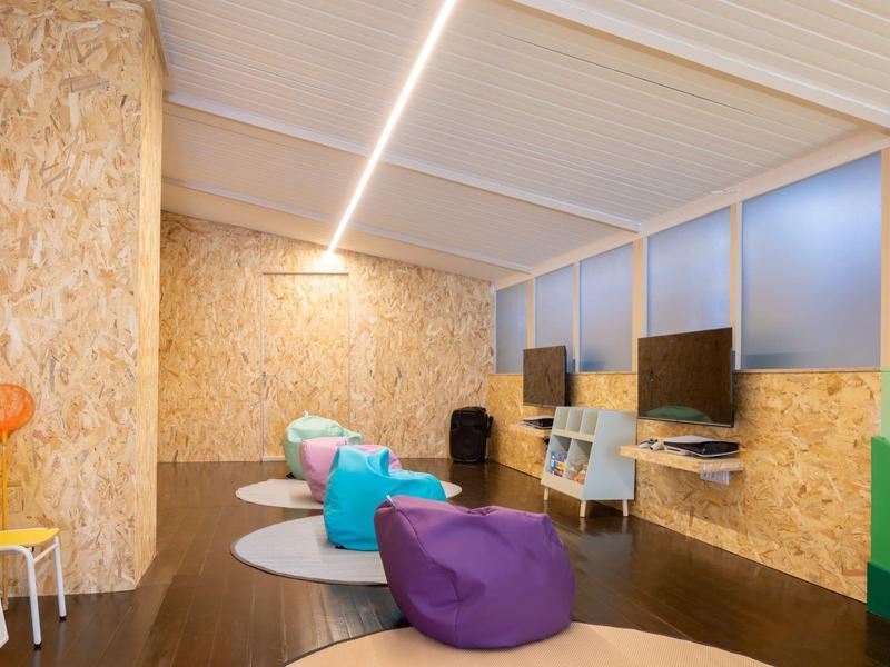 Area lounge moderna con pouf, computer e pannelli in legno alle pareti.