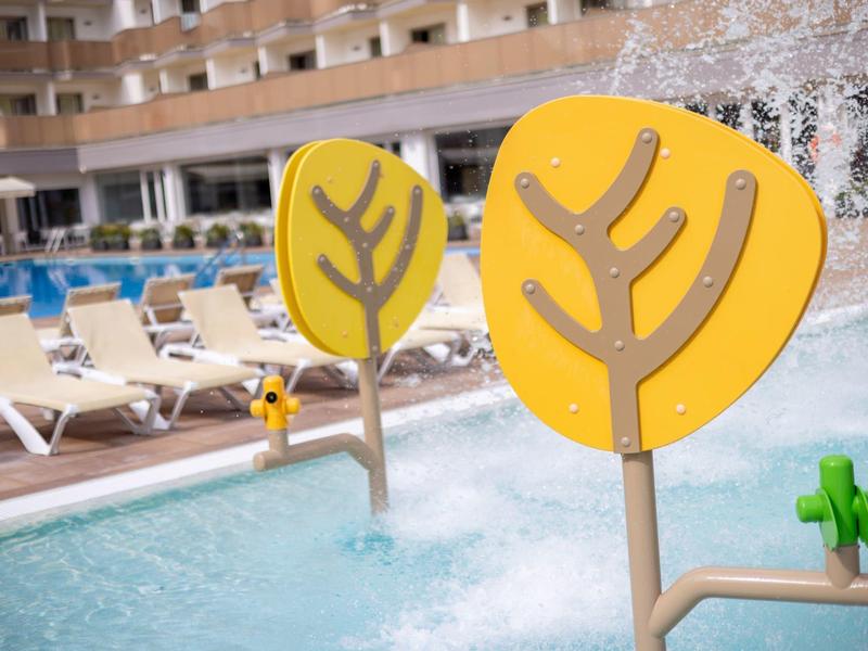 Sculture di alberi colorate nella piscina dell'hotel con sdraio e edificio a più piani sullo sfondo.
