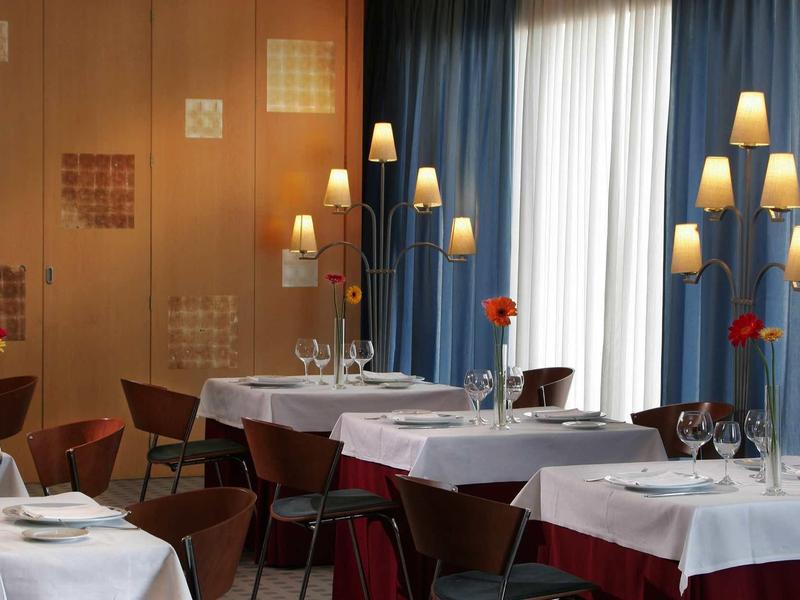 Ristorante elegante con tovaglie bianche, sedie moderne e illuminazione calda.