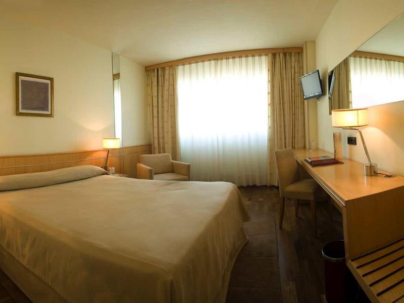 Camera d'hotel compatta con letto matrimoniale, scrivania, sedia e finestra con tende.