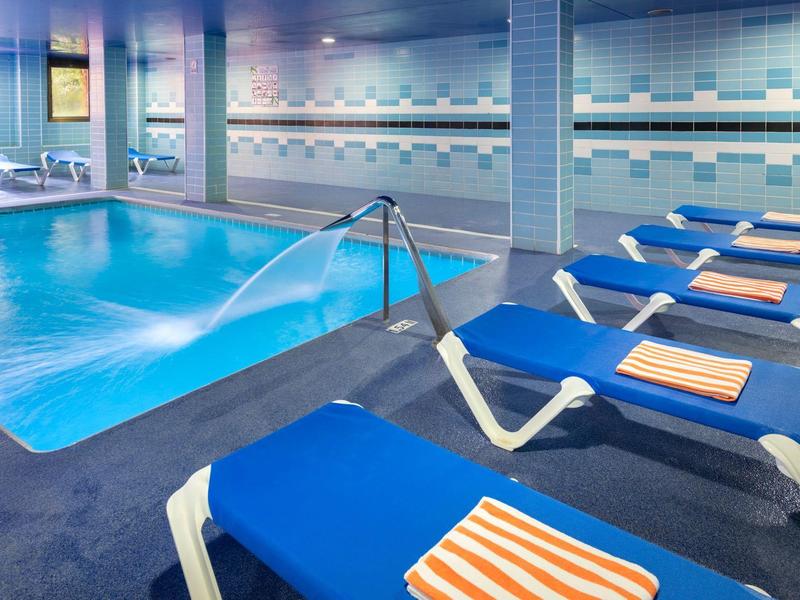 Binnenzwembad met blauwe ligstoelen en oranje gestreepte handdoeken in een hotel.