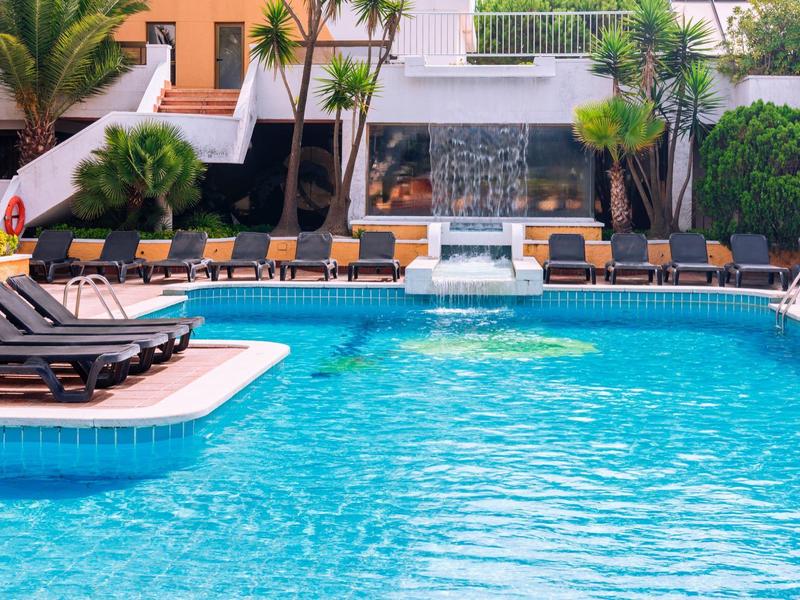 Verwarmd zwembad met ligstoelen en waterval in een tropisch hotel.