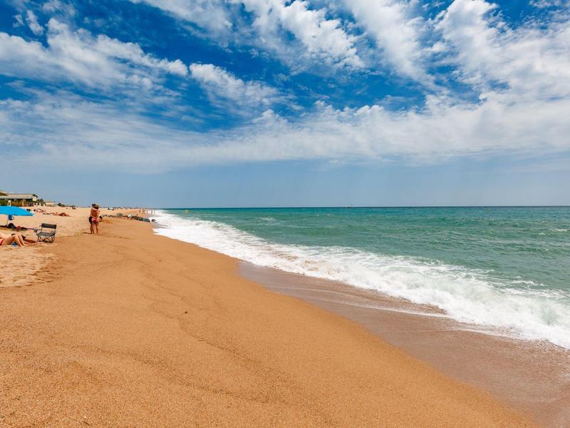 Breed zandstrand met zachte golven en een blauwe lucht met witte wolken.