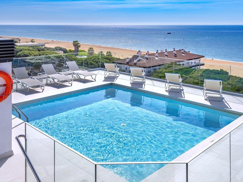 Dakterraszwembad met ligstoelen en uitzicht op zee bij heldere hemel.