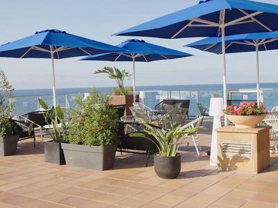 Terras met blauwe parasols, planten en uitzicht op zee bij het hotel.