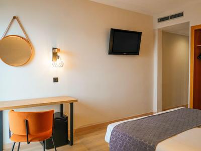 Moderne hotelkamer met bed, tv, grote spiegel en bureau met oranje stoel.