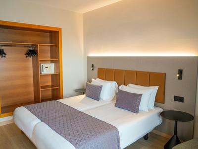 Modern hotelkamer met twee eenpersoonsbedden, hoofdwandverlichting en open garderobe.
