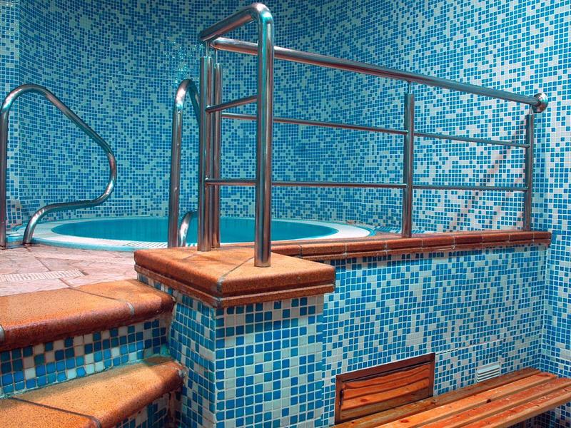 Piscina interior con azulejos de mosaico azul, escalones y barandilla de acero inoxidable.