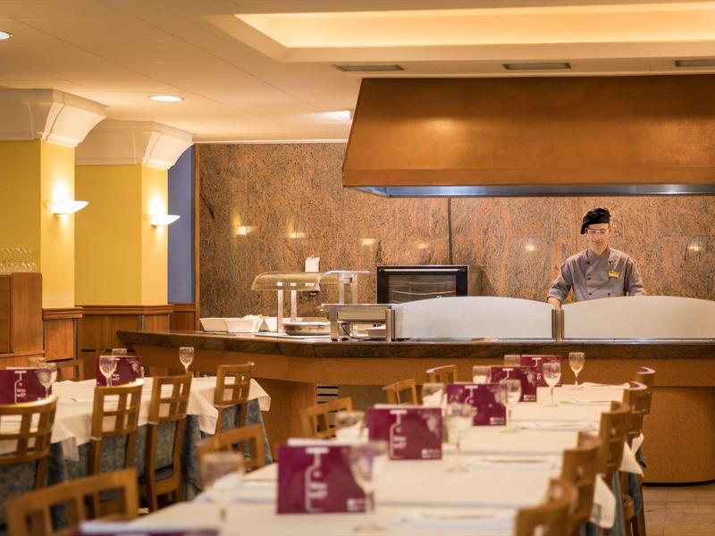 Restaurante acogedor con mesas preparadas y un chef detrás del mostrador.