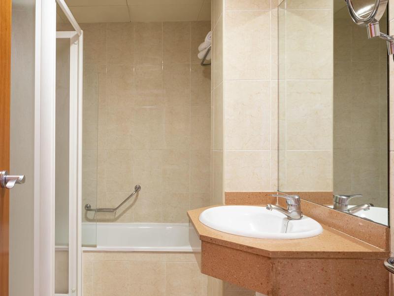 Pequeño baño con bañera, lavabo y gran espejo.