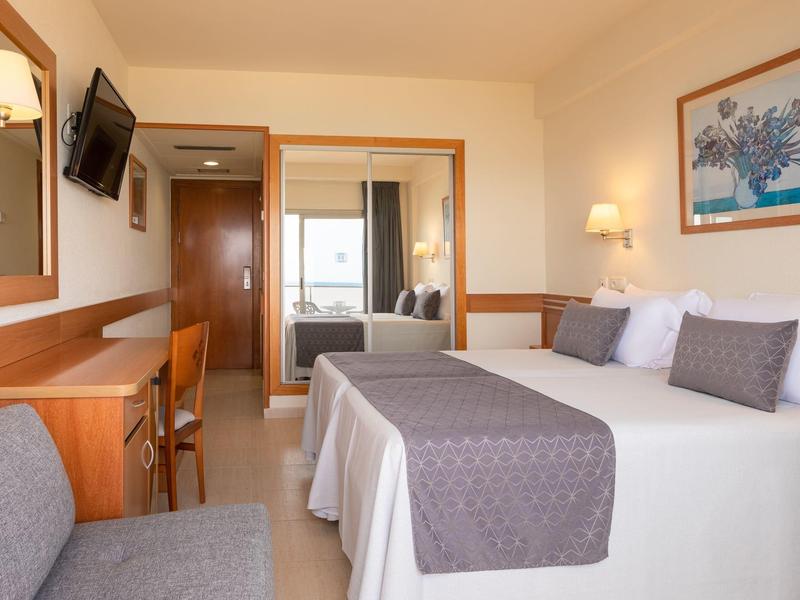 Habitación de hotel luminosa con cama doble, escritorio, TV y zona de estar.