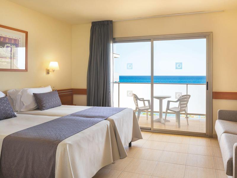 Habitación de hotel con dos camas, balcón con sillas y mesa, iluminación acogedora