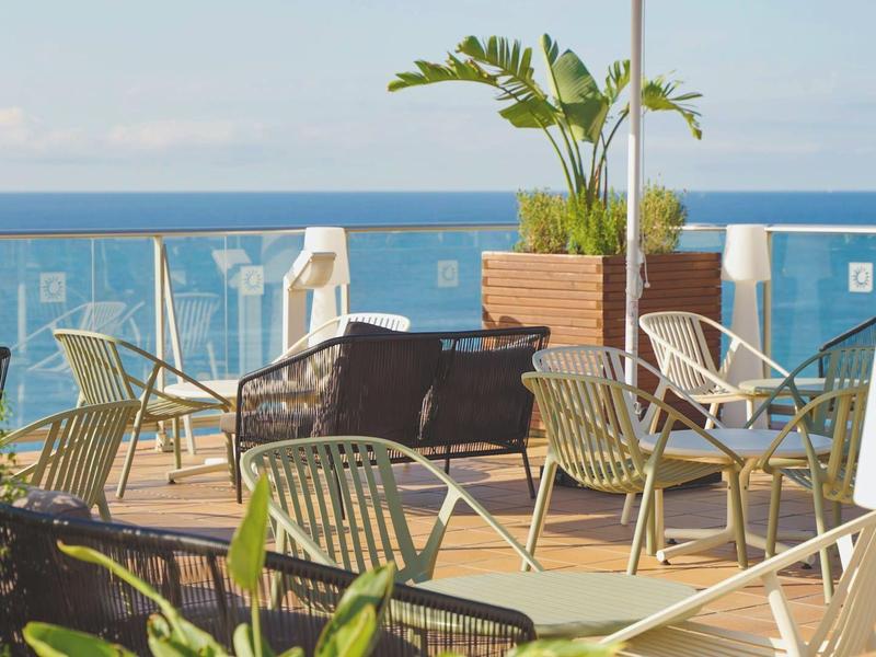 Terraza con mesas, sillas y plantas con vistas al mar abierto.