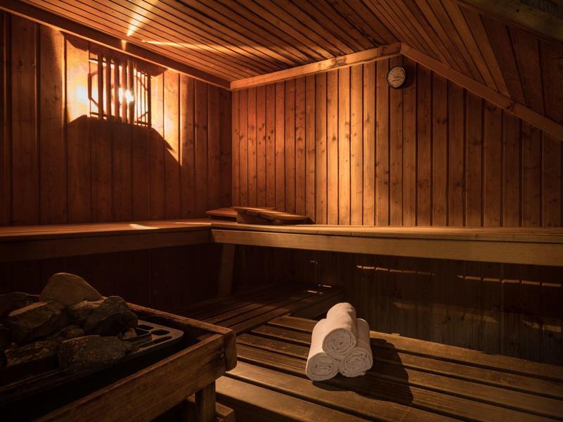 Sauna de madera con luz cálida y tres toallas blancas dobladas sobre un banco.