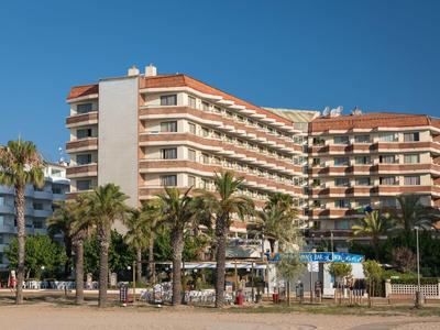 Mehrstöckiges Gebäude mit Balkonen und Palmen im Vordergrund bei klarem Himmel.