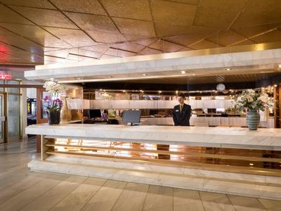 Große Hotelrezeption mit langen Marmor- und Holztheken, viel Platz und heller Beleuchtung.