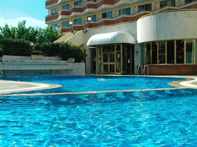 Modernes Hotelgebäude mit vielen Balkonen und klarem blauen Pool im Vordergrund bei sonnigem Wetter.