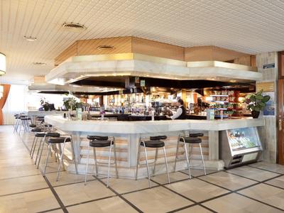 Moderner Barbereich mit weißen Tresen, schwarzen Hockern und großem Lüftungssystem an der Decke.